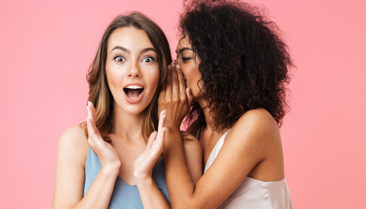 A woman tells a secret to her surprised friend