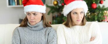 two white women wearing santa hats and sweaters sulking on the couch after an argument