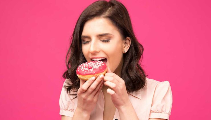 A brunette woman prepares to take a bite of a pink donut