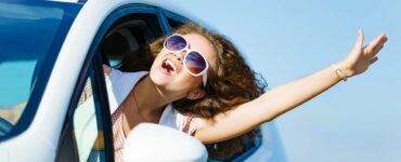 young woman leans out of the window while driving to enjoy the sunshine