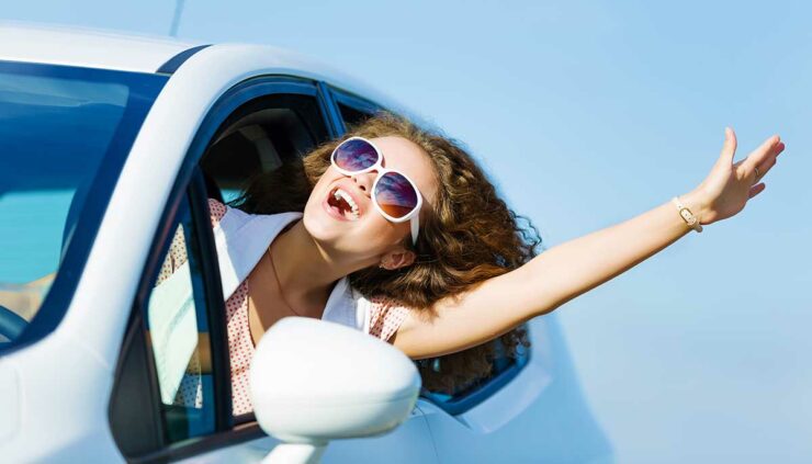 young woman leans out of the window while driving to enjoy the sunshine