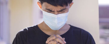 a young man wears a medical mask while he prays