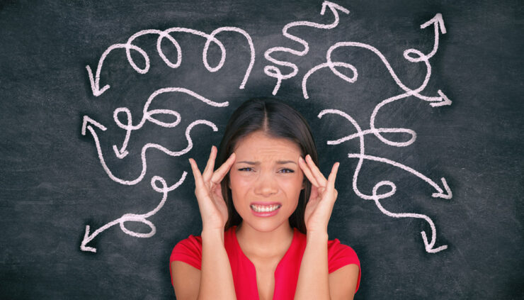 An asian woman in a red shirt stands in front of a chalkboard depicting confusing arrows sprouting out of her head.