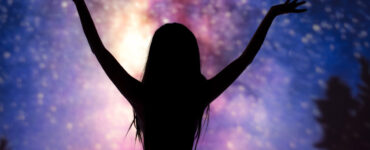 A silhouette of a woman raising her hands in enjoyment before a backdrop of stars.