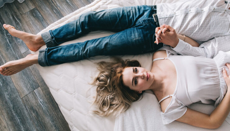 A woman in a white dress lays in bed next to a man flipped the opposite direction.