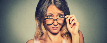 A woman wearing glasses stares skeptically at the camera.