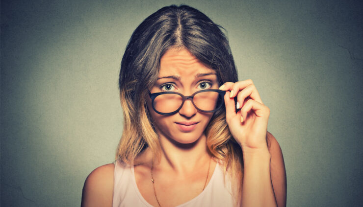 A woman wearing glasses stares skeptically at the camera.