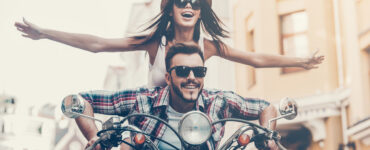 An attractive couple ride a motorcycle down a city street.