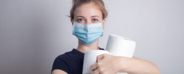 A woman in a mask holds an armful of toilet paper rolls.