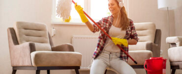 A woman in headphones dances with a mop while she cleans.