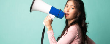 Asian woman holds a megaphone on a teal background.