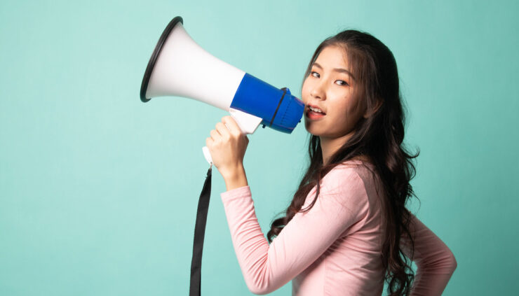 Asian woman holds a megaphone on a teal background.