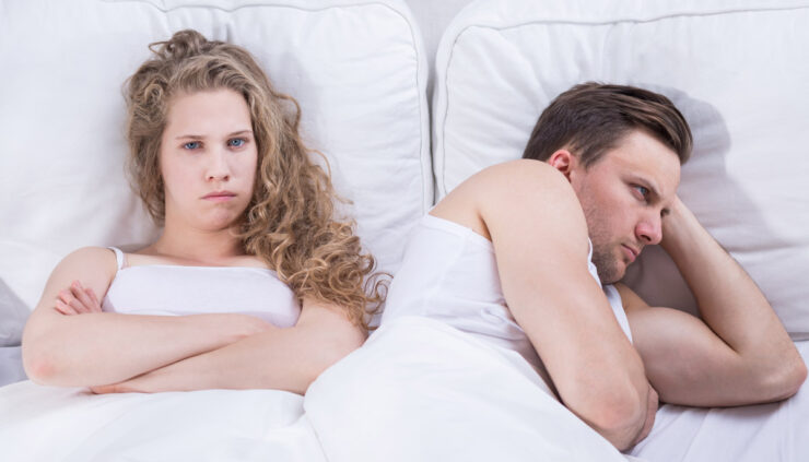 An angry and frustrated couple lying next to each other in bed.