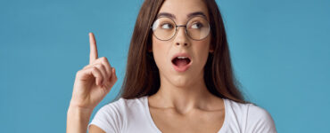 Brunette woman on blue background has an astonished expression and her finger pointed in the air.