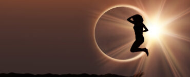 Silhouette of a woman jumping in front of a solar eclipse.