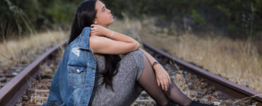 A young woman sits on train tracks staring off into the distance.