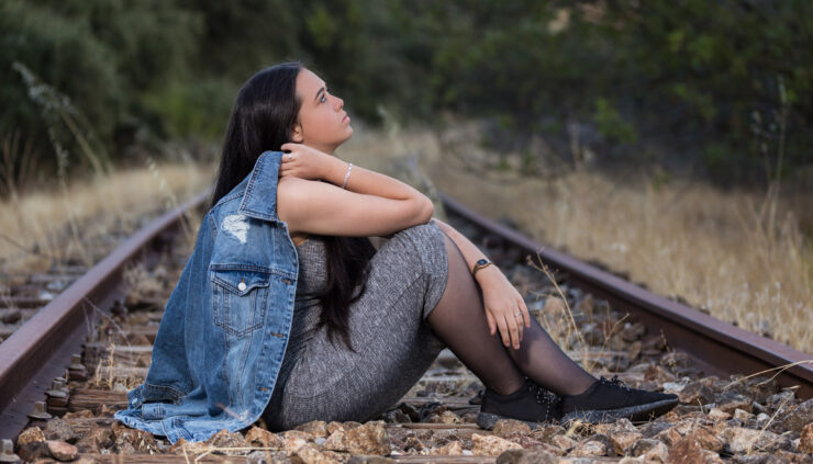 A young woman sits on train tracks staring off into the distance.