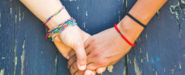 A caucasian and African American hold hands against a blue backdrop.