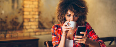 Attractive African American woman reads her phone while sipping coffee.