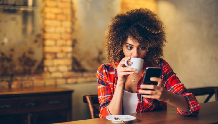 Attractive African American woman reads her phone while sipping coffee.