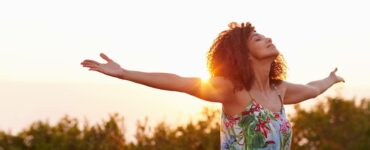 Beautiful African American woman raises arms in an open field at sunrise.