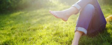 A woman wearing cuffed jeans relaxes on her back in a meadow.