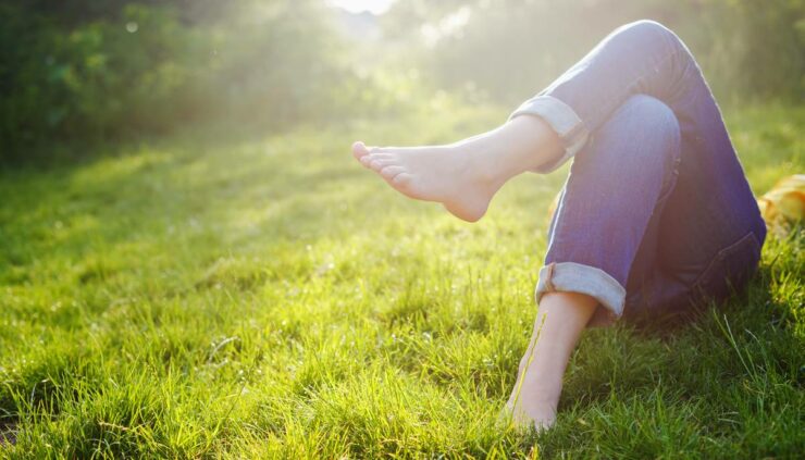 A woman wearing cuffed jeans relaxes on her back in a meadow.