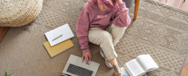 Pink haired girl works on her laptop on the floor.