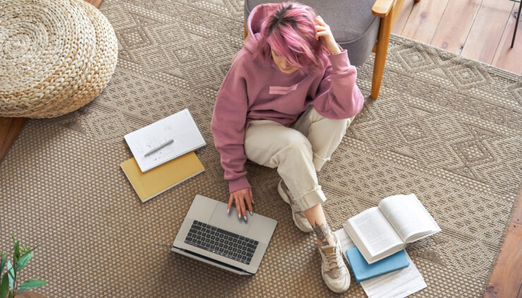 Pink haired girl works on her laptop on the floor.