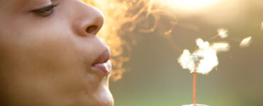 POC woman blowing a dandelion puff.