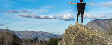 Woman stands on a cliff with her arms outstretched.