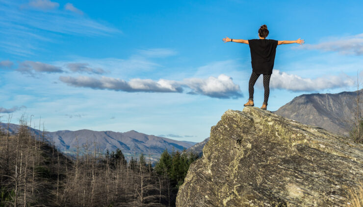 Woman stands on a cliff with her arms outstretched.