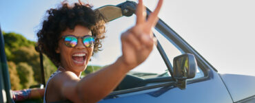 African American woman in a convertible flashes a peace sign at the camera