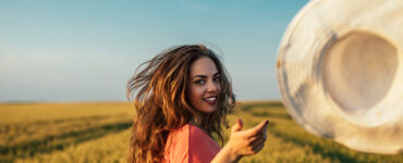 Woman in a field throws her hat at the camera.