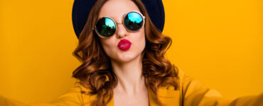 Red headed woman in sunglasses and red lipstick on a bright gold background.