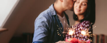 man-kisses-woman-on-cheek-while-they-hold-sparkler-cupcakes