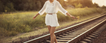 Young woman holding flowers balancing on a railroad beam