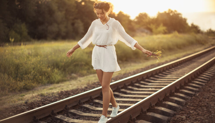 Young woman holding flowers balancing on a railroad beam