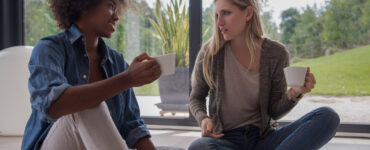 Two women talk while sitting on the floor