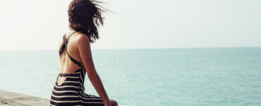 Dark haired woman sitting on pier looking at ocean