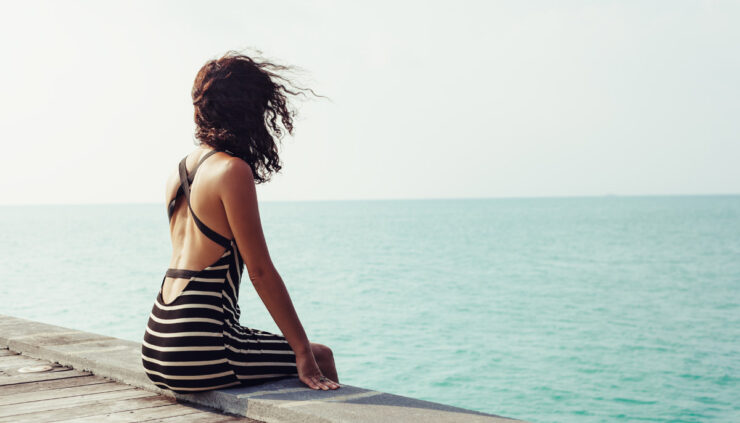Dark haired woman sitting on pier looking at ocean