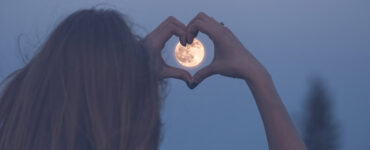 Woman forming a heart with her hands around a moon