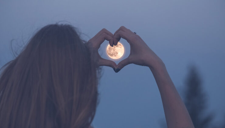 Woman forming a heart with her hands around a moon