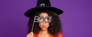 Woman wearing a witch's hat and holding up a sign that says "boo!"