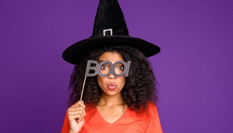 Woman wearing a witch's hat and holding up a sign that says "boo!"