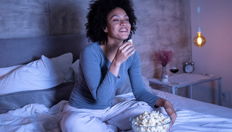 woman-eats-popcorn-and-laughs-in-bed