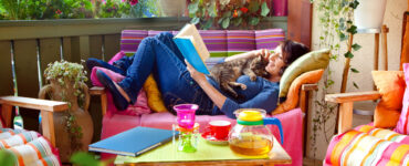 Woman reading book and cuddling cat on colorful porch