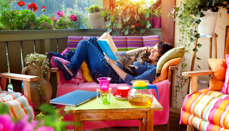 Woman reading book and cuddling cat on colorful porch